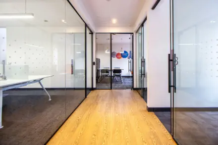 Agencement de bureaux en Île-de-France : Couloir de bureau moderne avec cloisons vitrées et sol en parquet bois clair.