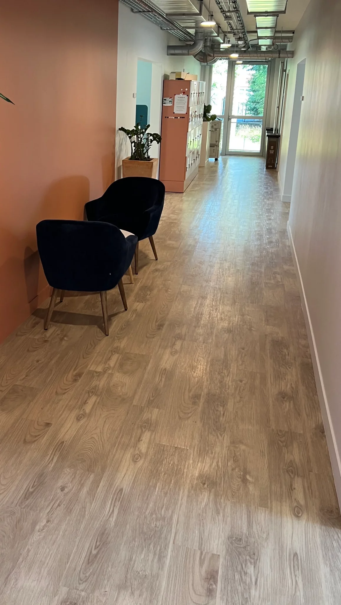 Projets d’aménagement et de réaménagement tertiaire : sol en parquet stratifié clair, fauteuils bleu marine et mur couleur terracotta dans un espace de travail contemporain